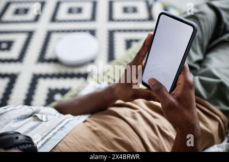 High angle view closeup of unrecognizable Black man sitting in living room using robotic vacuum cleaner app on smartphone Stock Photo