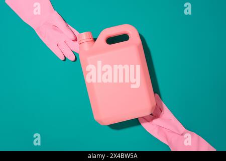 An unlabeled bottle of detergent and a pair of rubber gloves on a turquoise background. Mockup of cleaning products for advertising. Top view. Stock Photo
