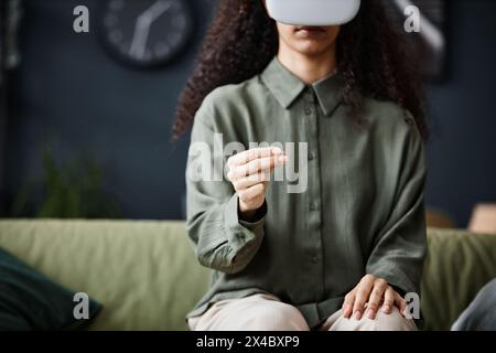 Medium crop shot of unrecognizable woman sitting on sofa in living room using VR headset, copy space Stock Photo
