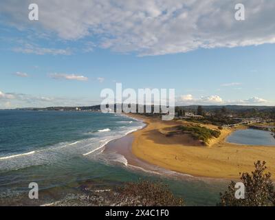 Panoramic view of the beach at Narrabeen, in Sydney, Australia, on a cloudy day with rough seas and orange sands and dunes leading to a small lagoon Stock Photo