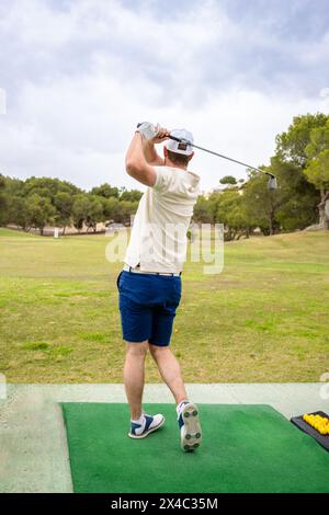 Young man wearing cap playing golf against clear sky at golf course Stock Photo