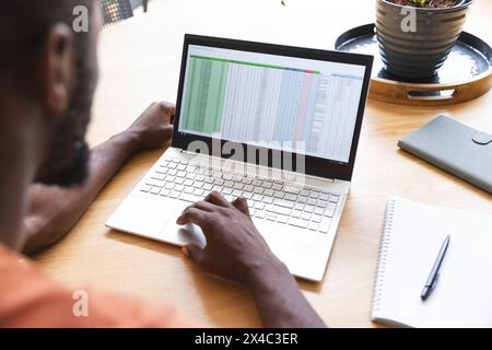 An African American male studying spreadsheet on laptop at home. Wearing casual clothes, focusing on screen, with short hair and thoughtful look, unal Stock Photo