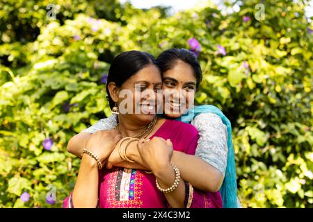 Indian mother and daughter in traditional attire, embracing outside. Both with black hair, smiling, enjoying warm moment together, unaltered Stock Photo