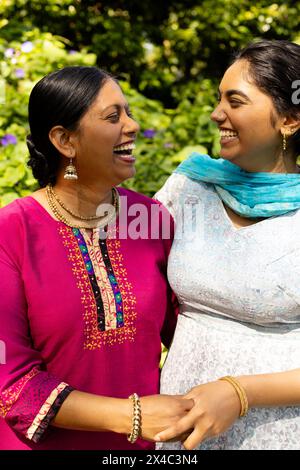 Indian mother and teenage daughter laughing together outdoors. Both sporting dark hair, with mother's cut short and daughter's long, unaltered Stock Photo