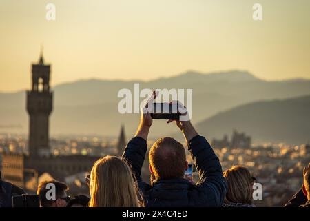 A crowd of tourists holding phones over their heads to take photos of the Florence skyline at Piazzale Michelangelo. An example of overtourism. Stock Photo