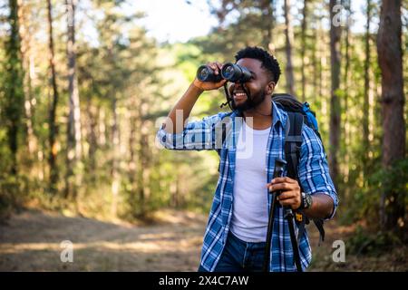 Young man enjoys using  binoculars and hiking  in nature. Stock Photo