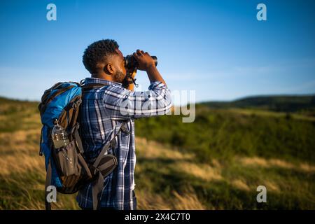 Young man enjoys using  binoculars and hiking  in nature. Stock Photo