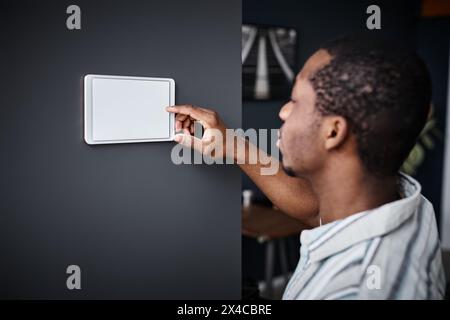 Closeup of young Black man adjusting indoor temperature with use of smart home system Stock Photo