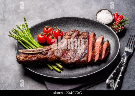 Medium rare grilled Tomahawk beef steak with asparagus on plate Stock Photo