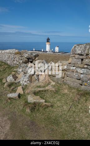 Dunnet Lighthouse and light keeper cottages framed by a damaged dry stone wall. Stock Photo
