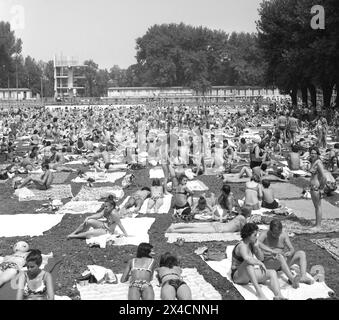 Bucharest, Socialist Republic of Romania in the 1970s. Hundreds of people sunbathing at a local pool, one of the very few ways of spending a good time in the summer in the capital city. On the building in the back there is a large communist banner saying 'Long live The Socialist Republic of Romania'. Stock Photo