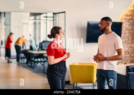 Young business colleagues, including an African American businessman, engage in a conversation about business issues in the hallway of a modern Stock Photo