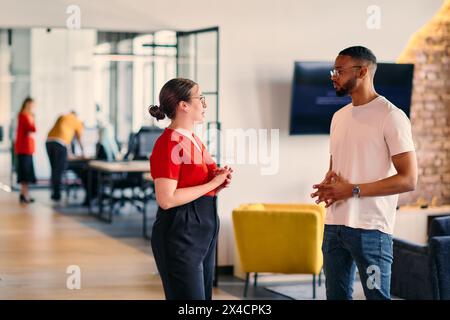 Young business colleagues, including an African American businessman, engage in a conversation about business issues in the hallway of a modern Stock Photo