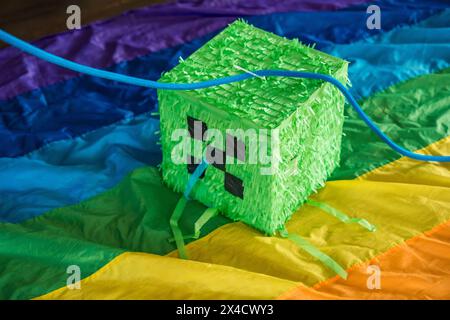 Green cube pinata in pixel craft style on rainbow background for kids birthday party Stock Photo