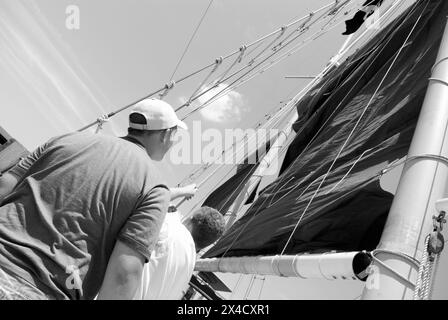 Two boys raise the sail on the Jolly Rover tall ship, docked on the riverfront in Georgetown, South Carolina, USA. Stock Photo