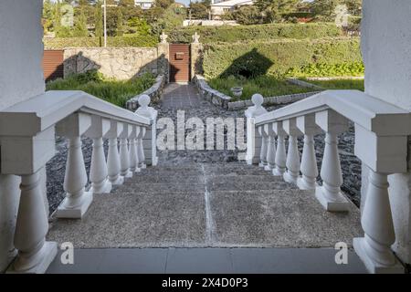 Exterior stairs of a single-family home with white prefabricated balustrades leading to a paved hallway with concrete steps Stock Photo