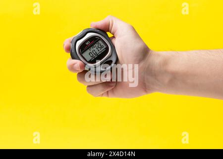 Man hand holding stopwatch on yellow background, closeup. Time management concept Stock Photo