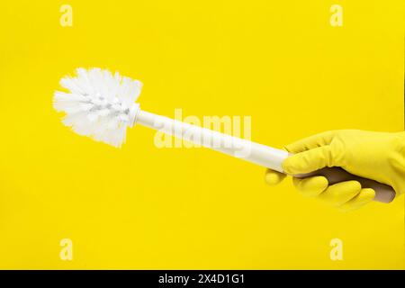 Hand in yellow rubber glove holding a cleaning brush on a yellow background Stock Photo