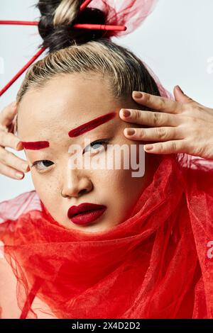 Asian woman, hands on head, wearing red dress, poised gracefully. Stock Photo