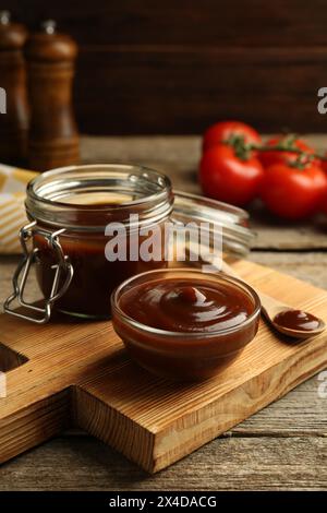 Tasty barbeque sauce in bowl, jar and spoon on wooden table Stock Photo