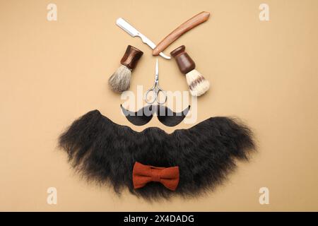 Artificial moustache, beard and barber tools on beige background, flat lay Stock Photo