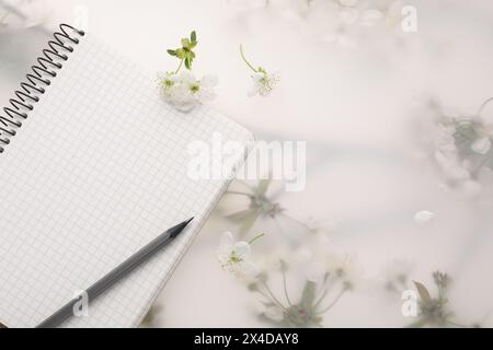 Guest list. Notebook, pencil and beautiful cherry tree blossoms on spring floral background, flat lay. Space for text Stock Photo