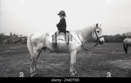 1960s, historical, a young girl sitting backwards, arms folded, on a horse outside in a field at a riding school, a technique used to improve a rider's balance. Stock Photo
