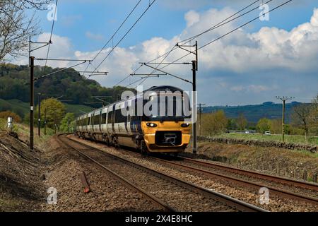 A Northern electric train approaches a foot crossing over the railway at the end of Parkers Lane in Low Utley in the Aire valley in West Yorkshire. Stock Photo