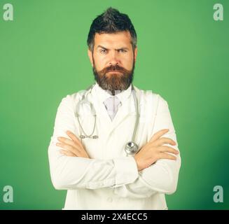 Profession, medicine, healthcare and medical staff concept. Handsome bearded intern, physician in white uniform with crossed arms in clinic. Serious Stock Photo