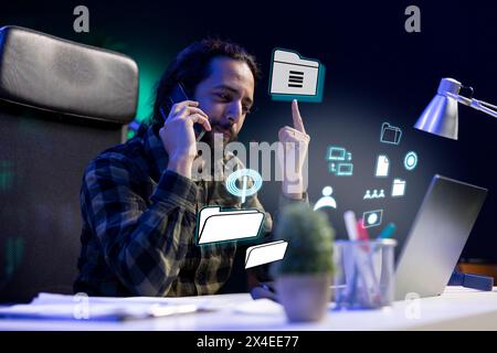 Smiling man talking on phone with coworker, working on laptop, accessing digital information concept. Employee using AR tech to interact with notebook, chatting over telephone call Stock Photo