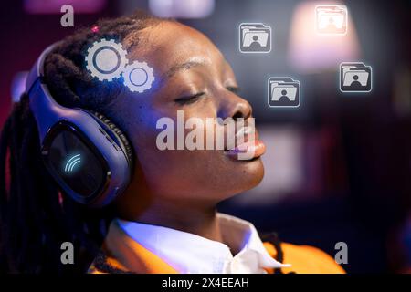 African american woman at home closing eyes, using futuristic headphones and AR technology to control software with mind. BIPOC person using audio headset and augmented reality tech to be immersed Stock Photo