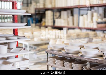 Unfinished ceramic bowls and plates organized on racks in pottery studio Stock Photo