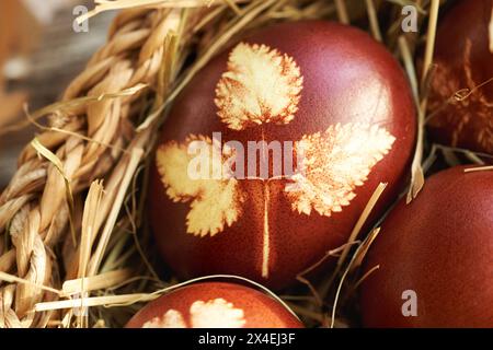 Close up of brown Easter eggs dyed with onion peels with a pattern of fresh leaves in a wicker basket Stock Photo