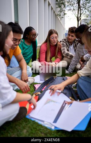 Group of young international students sitting on the grass outside the university building Stock Photo