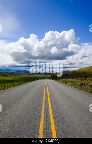 Two lane road in Eastern Oregon with double yellow lines leading to big white clouds above highway in remote landscape of Pacific Northwest Stock Photo