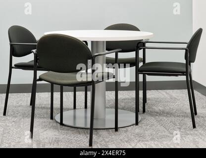Round table four black chairs in office setting gray carpet no people. Stock Photo