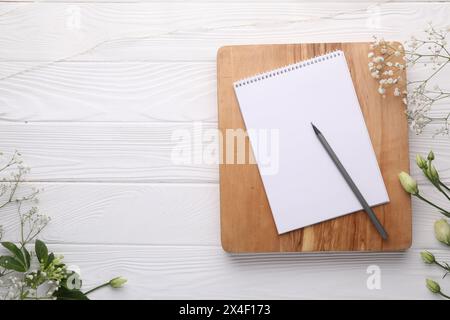 Guest list. Notebook, pencil and beautiful flowers on white wooden background, flat lay. Space for text Stock Photo