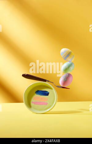 The front of a round tray with colored stripes is holding up colorful eggs on a yellow background. Creative ideas for Easter decoration. Space for des Stock Photo