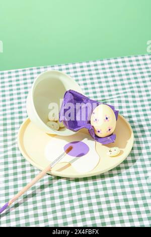 On a pastel green background and checkered plain, a round dish with Easter eggs, brush and purple blister decorated. Easter celebration concept Stock Photo