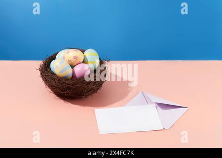 A nest filled with colorful eggs on a blue background decorated with cards. A meaningful gift for Easter. Space for design card. Minimal scene for adv Stock Photo