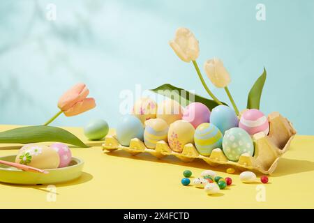 Easter party concept. Colorful Easter egg tray decorated with tulips on pastel blue and yellow background. Front view, make your own meaningful gifts Stock Photo