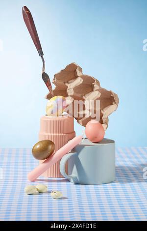 On light blue background and checkered plain, Easter eggs and Easter candle decorated with ceramic cups. Creative advertising photo. Front view Stock Photo