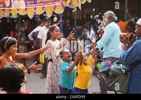 Joyful children dance while a street vendor blows soap bubbles. Bainan Bazaar area, Bagnan, Howrah, West Bengal, India. Stock Photo