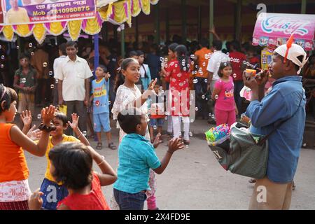 Joyful children dance while a street vendor blows soap bubbles. Bainan Bazaar area, Bagnan, Howrah, West Bengal, India. Stock Photo