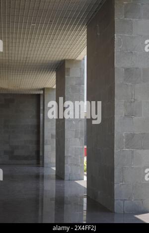 A dark hallway with gray square pillars with a light source from between Stock Photo