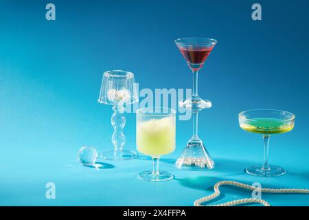 Front view of glass cups with delicious drinks decorated on blue background with glass ball and pearl necklace. Creative scene for advertising product Stock Photo