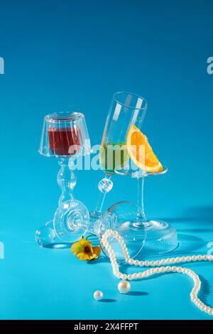 Holiday concept with glass cup container red and green liquid, orange slices and pearl necklace decorated on a blue background. Front view, scene for Stock Photo