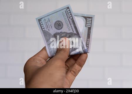 Closeup image of hand holding 100 US dollar banknotes against white wall. Stock Photo