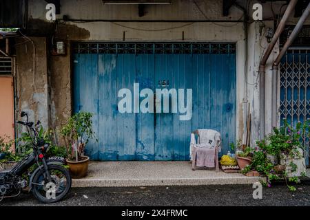 A rustic scene with a vintage motorcycle parked beside a weathered blue door, framed by potted plants and urban textures. Stock Photo