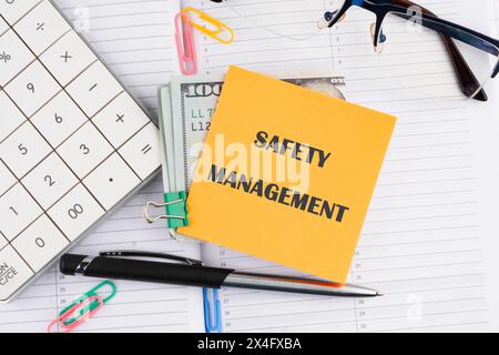 Business concept. SAFETY MANAGEMENT text written on a yellow sticker with money on a business notebook Stock Photo